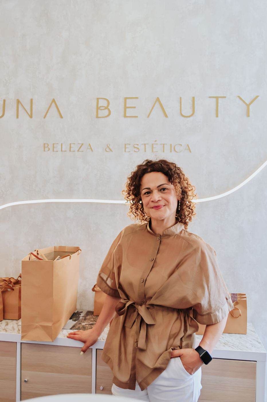 Fundadora da Una Beauty no salão, em frente ao letreiro dourado